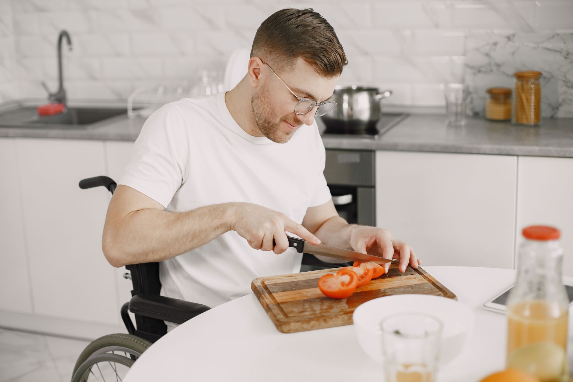 Man using a wheelchair slicing tomatoes at the bench in his own kitchen at home