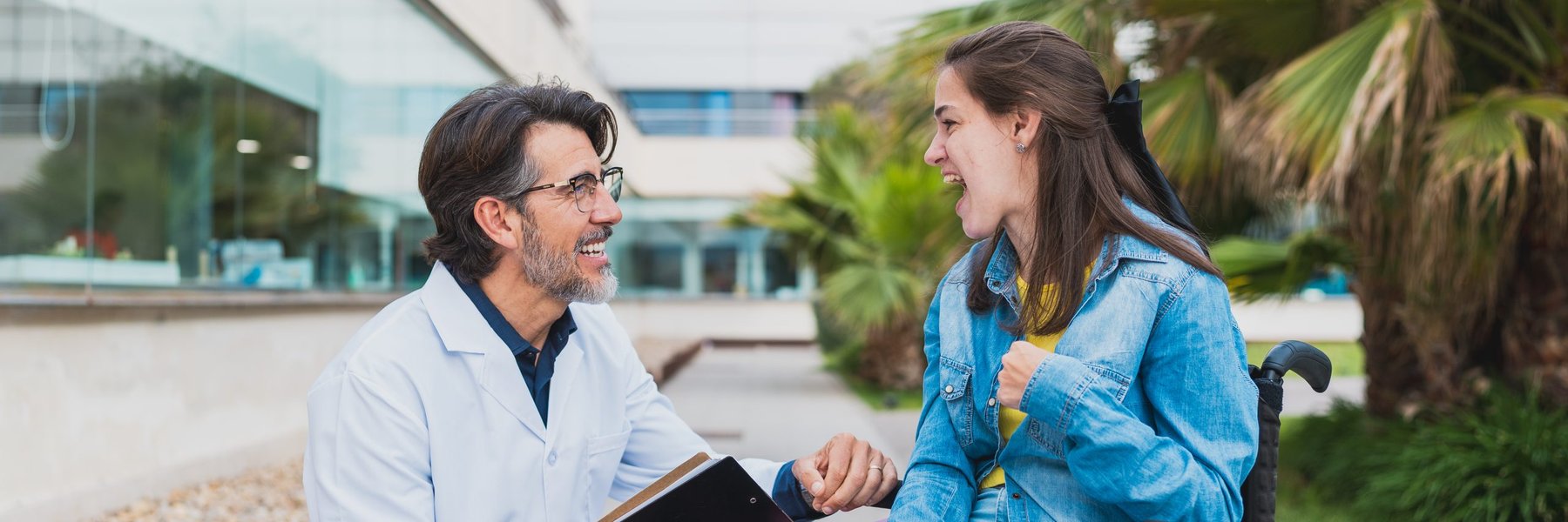 Healthcare professional and young woman with cerebral palsy smiling during a speech therapy consultation outdoors