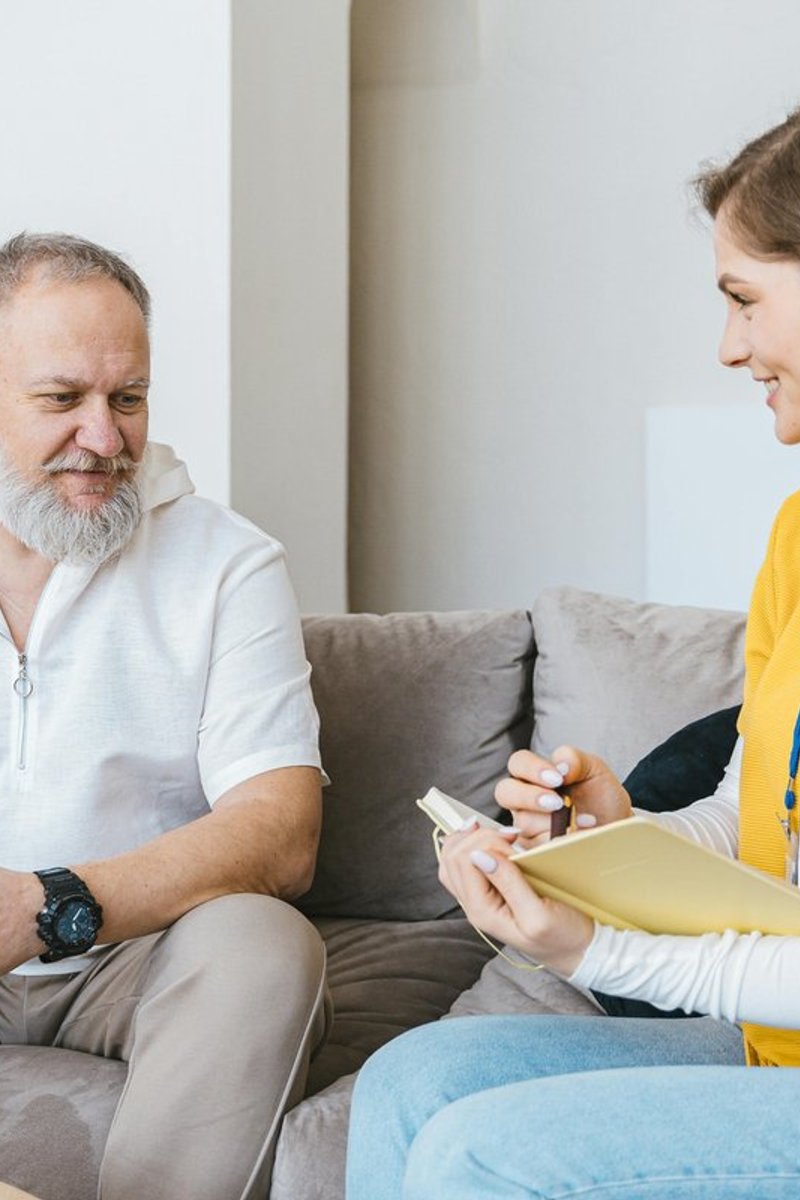 Healthcare professional consulting with an elderly man at home, taking notes during a falls prevention risk assessment