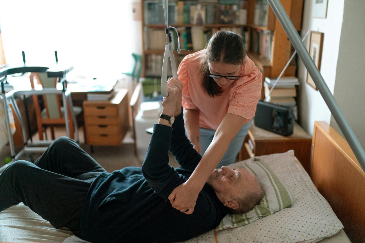 Healthcare professional assisting elderly man during home care occupational therapy visit