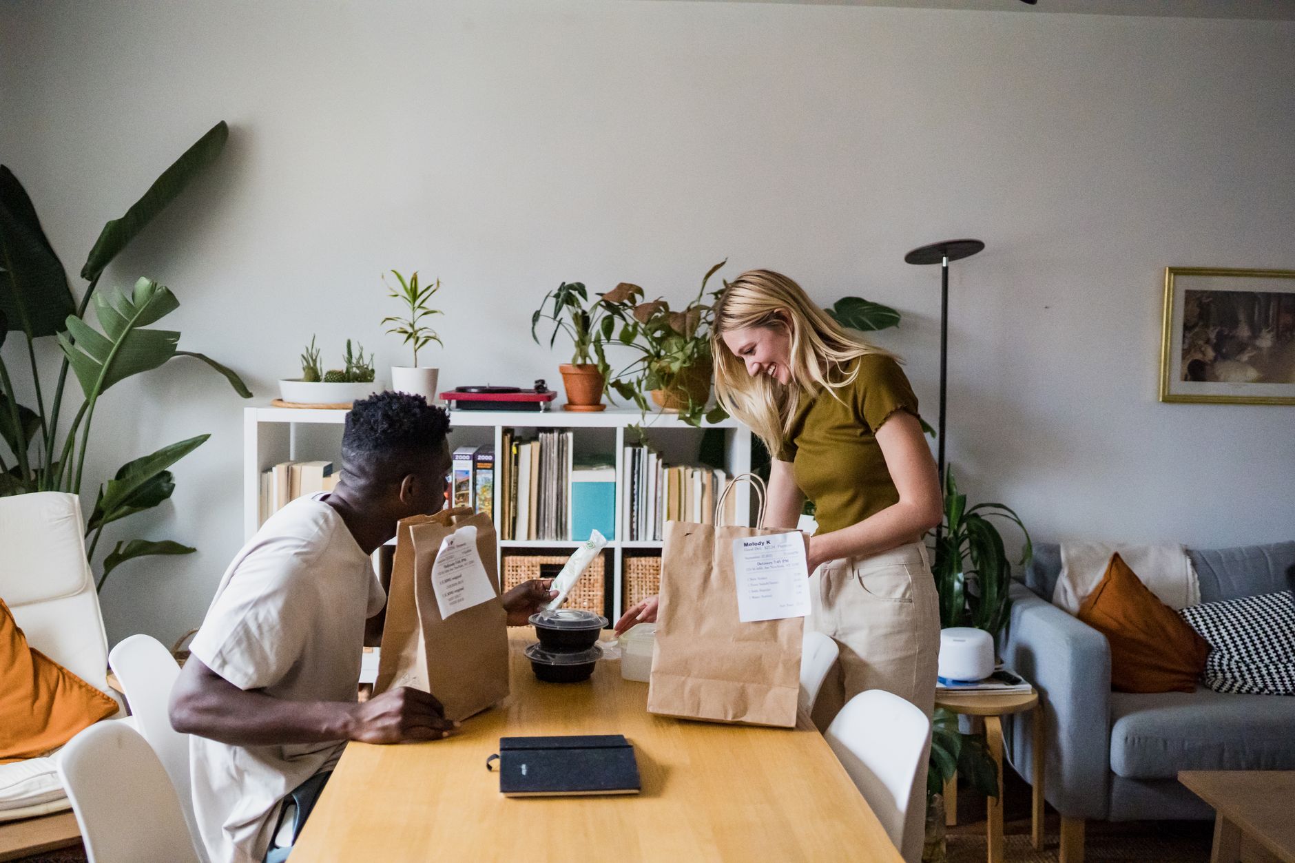 Two housemates unpacking a meal together at the dining table in their shared home