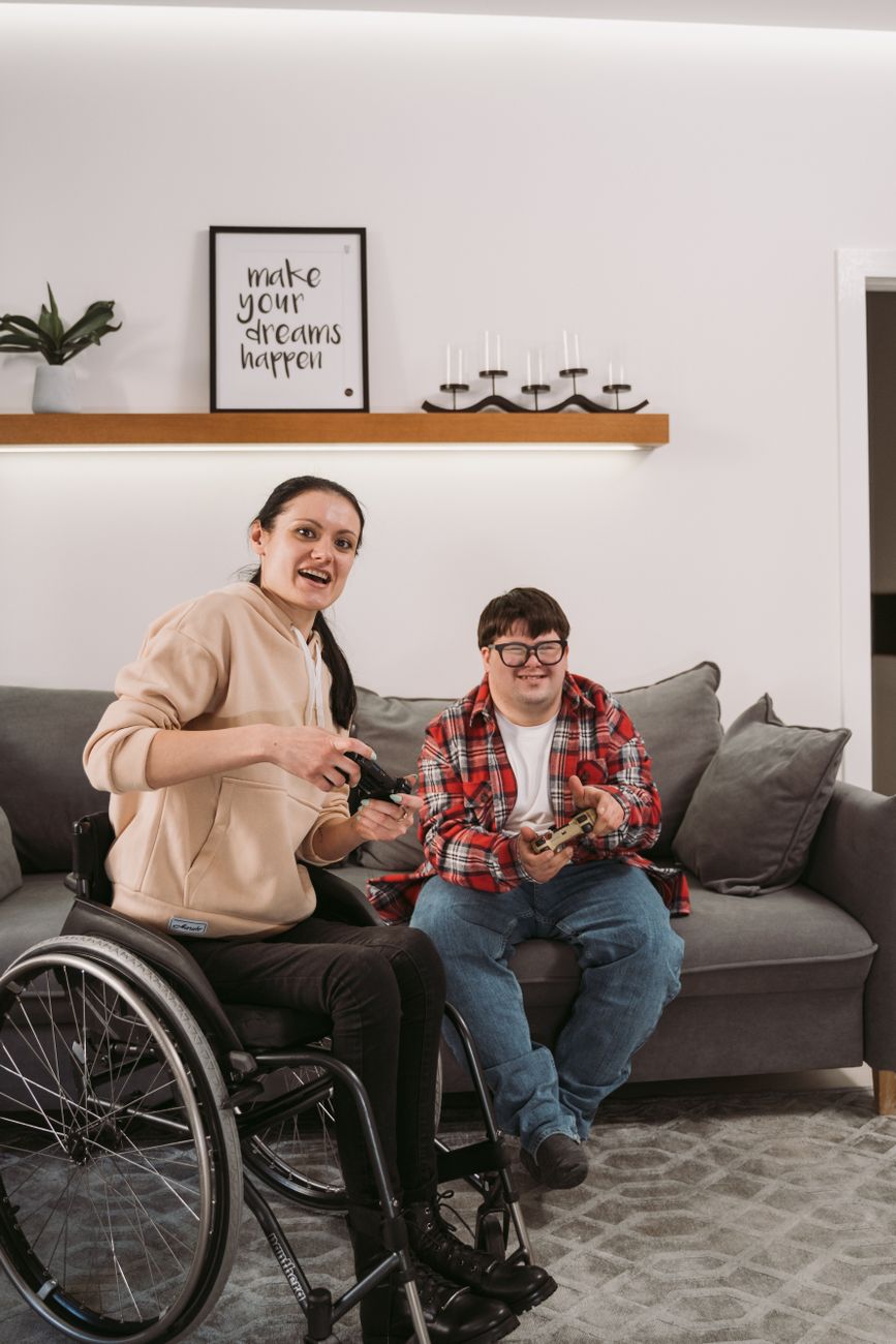 Two adults relaxing together in their shared living room, one using a wheelchair, showing the kind of home life Individualised Living Options funding is built around