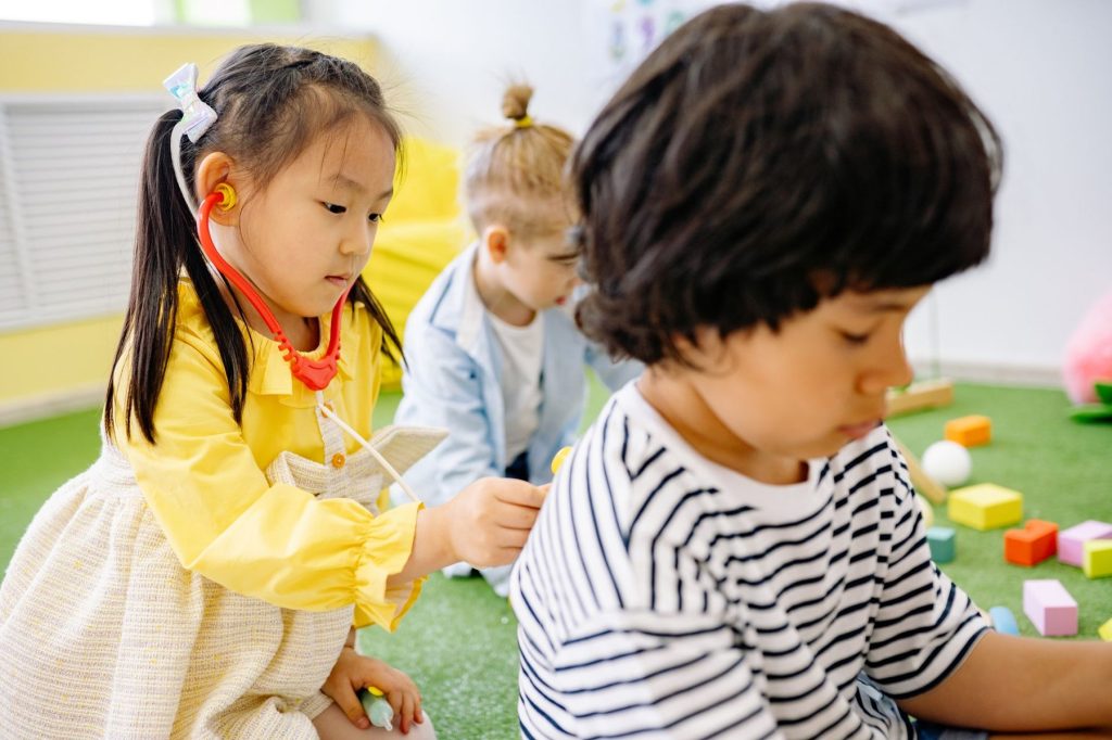 Young children engaged in pretend doctor play together in a bright early learning playroom, supporting social and communication development