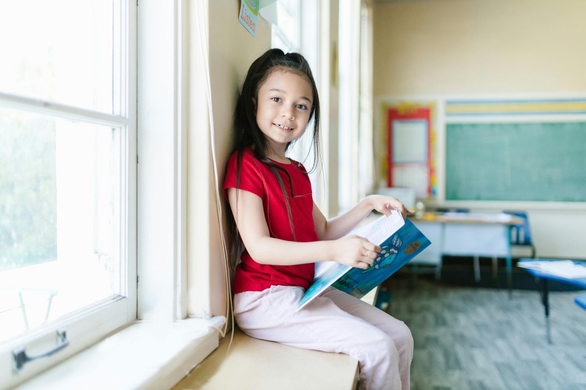 Happy child smiling while reading a book in a classroom, representing literacy support for children