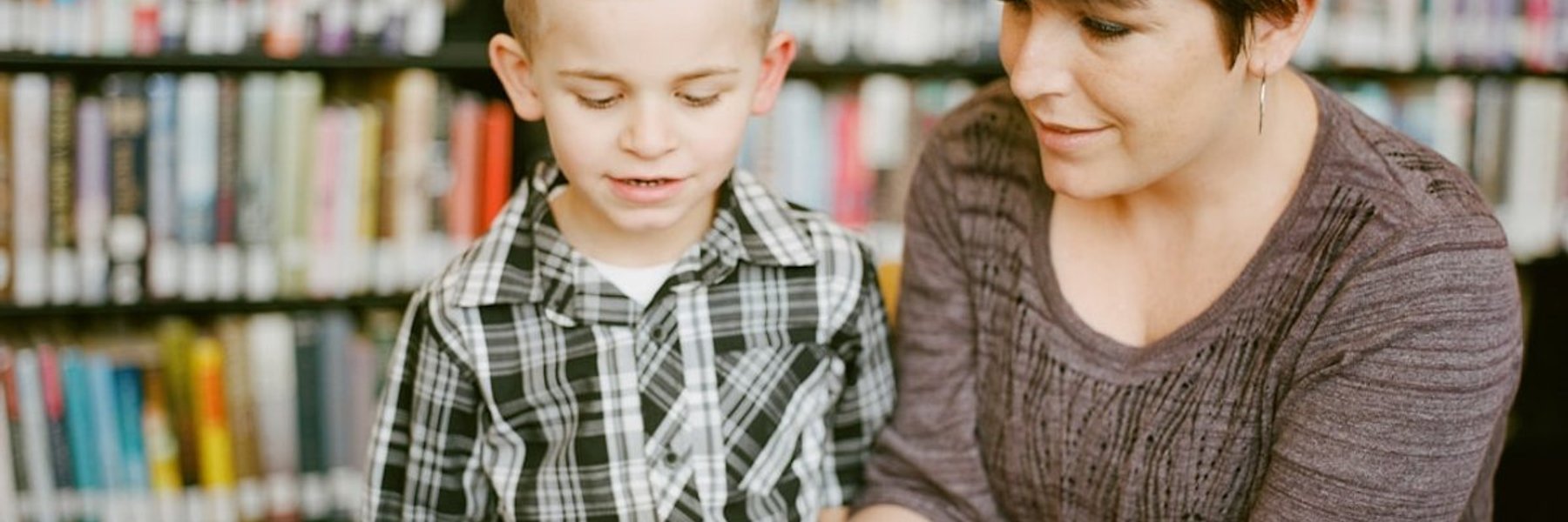 Child reading a book with an adult during a literacy assessment session at ASTRAD Allied Health