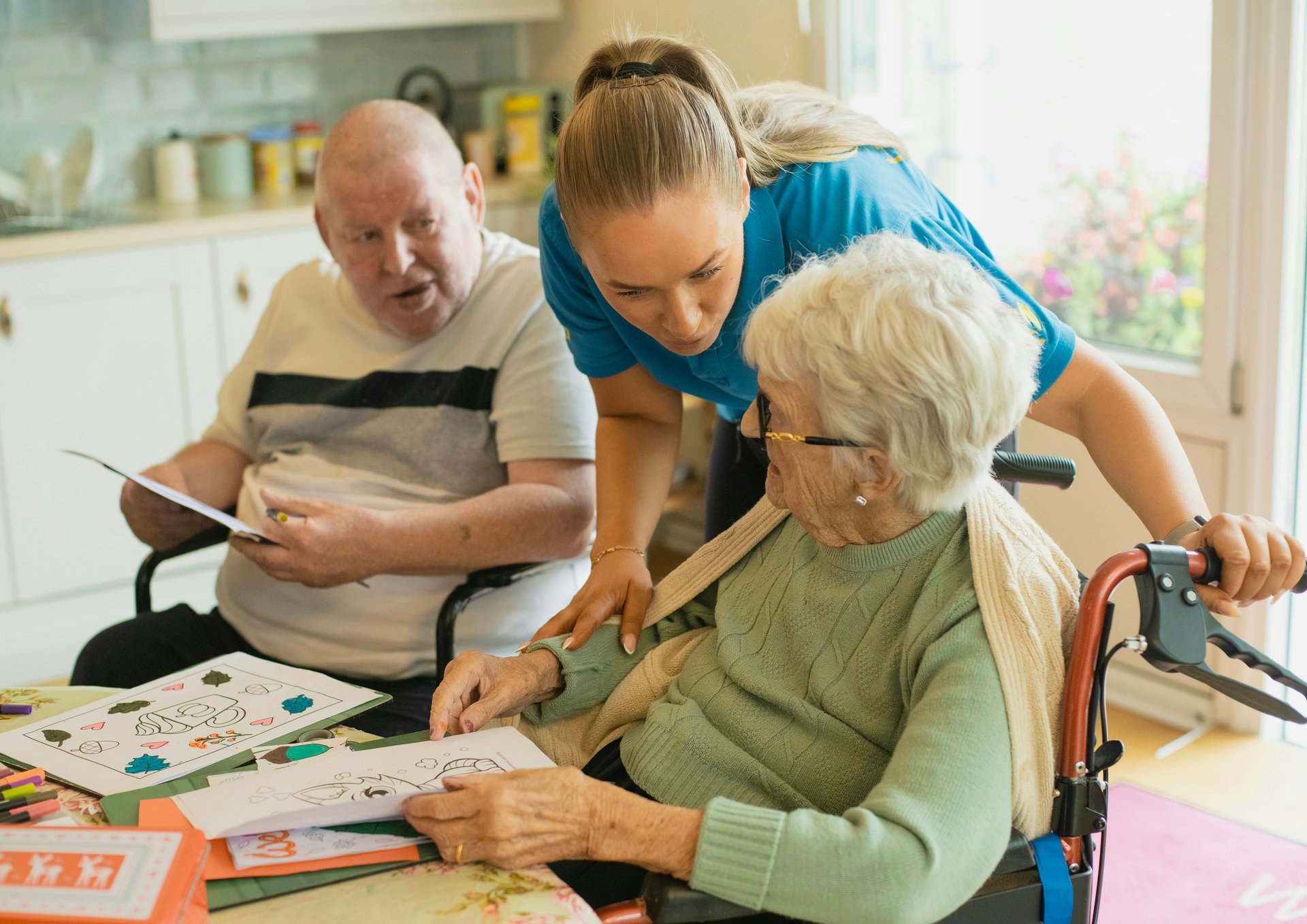 Mobile allied health worker supporting an older client with an activity at a home kitchen table