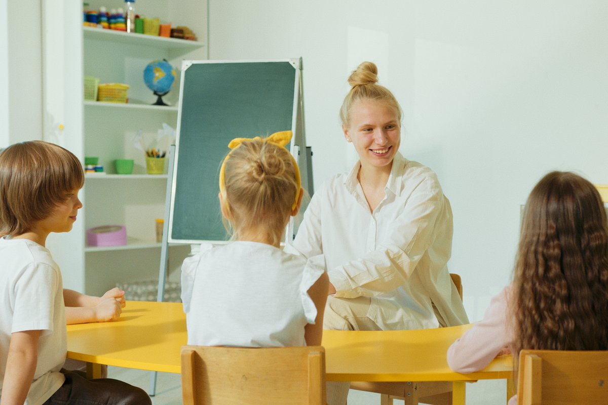 Speech pathologist smiling and engaging with young children during an NDIS-funded communication therapy session in a bright classroom setting