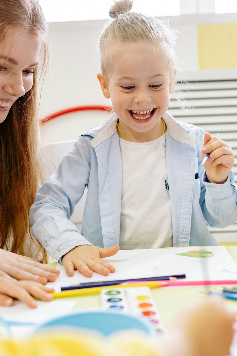 Happy young child laughing while participating in a creative speech therapy activity with a therapist