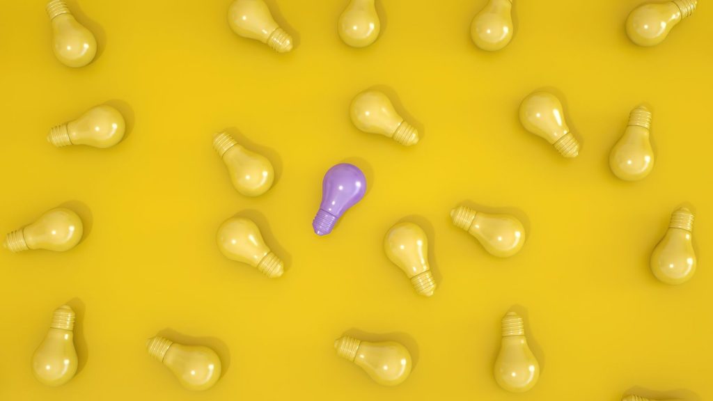 A single purple light bulb among yellow light bulbs on a yellow background, representing neurodivergent thinking and different ways of processing the world