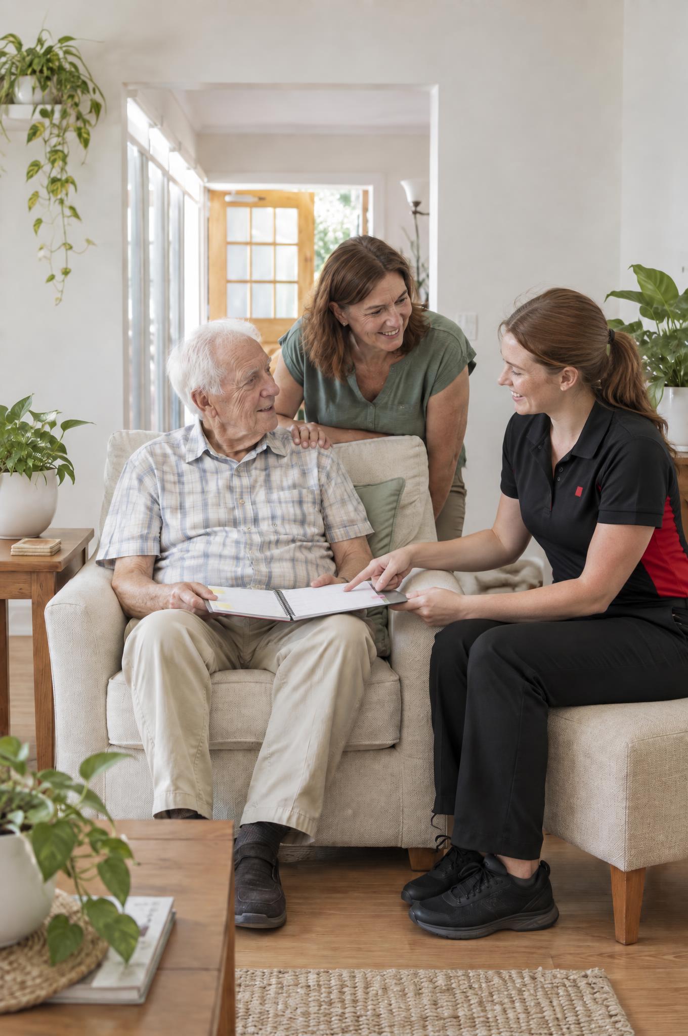 Occupational therapist going through a weekly planner with an older man in his armchair while his daughter looks on