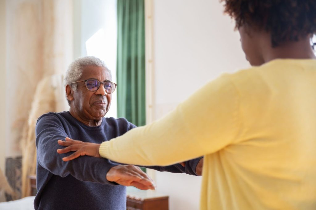 Occupational therapist guiding an elderly man through arm exercises during a home visit