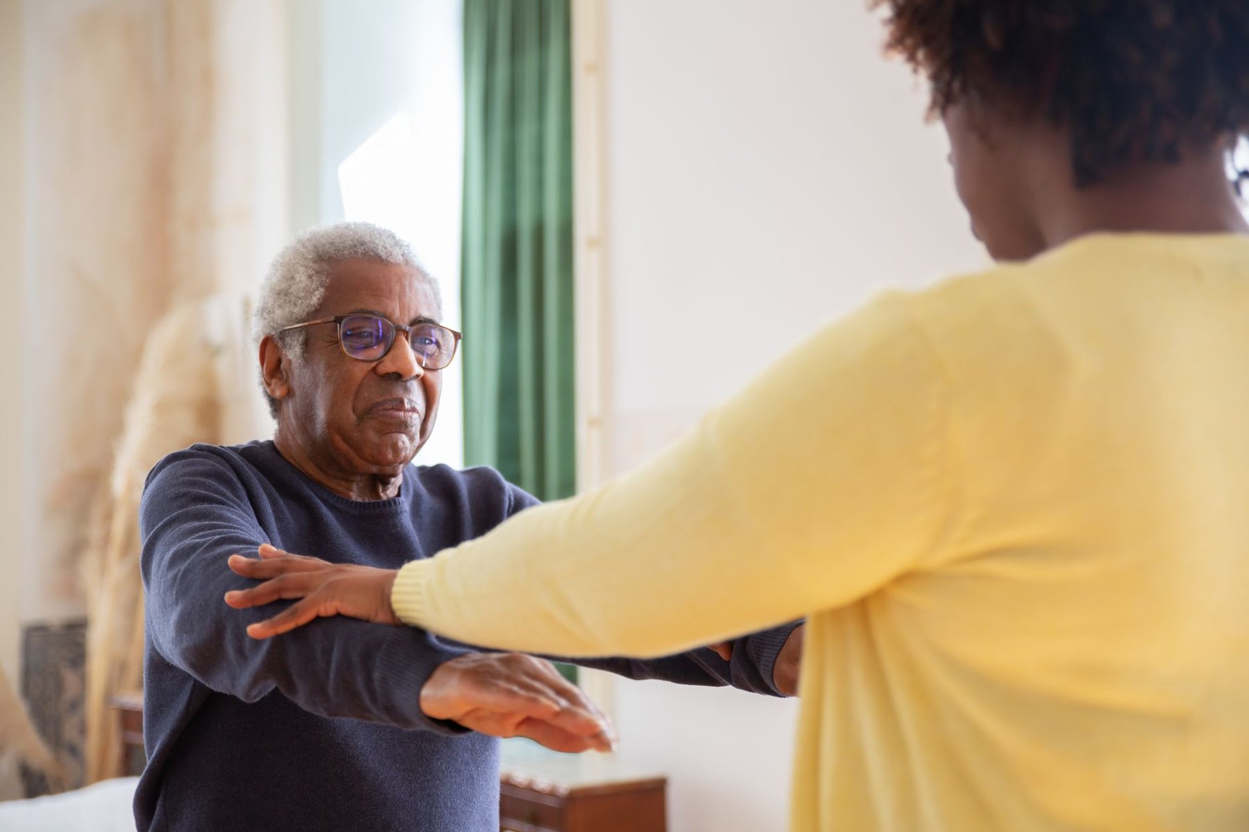 Occupational therapist guiding an elderly man through arm exercises during a home visit