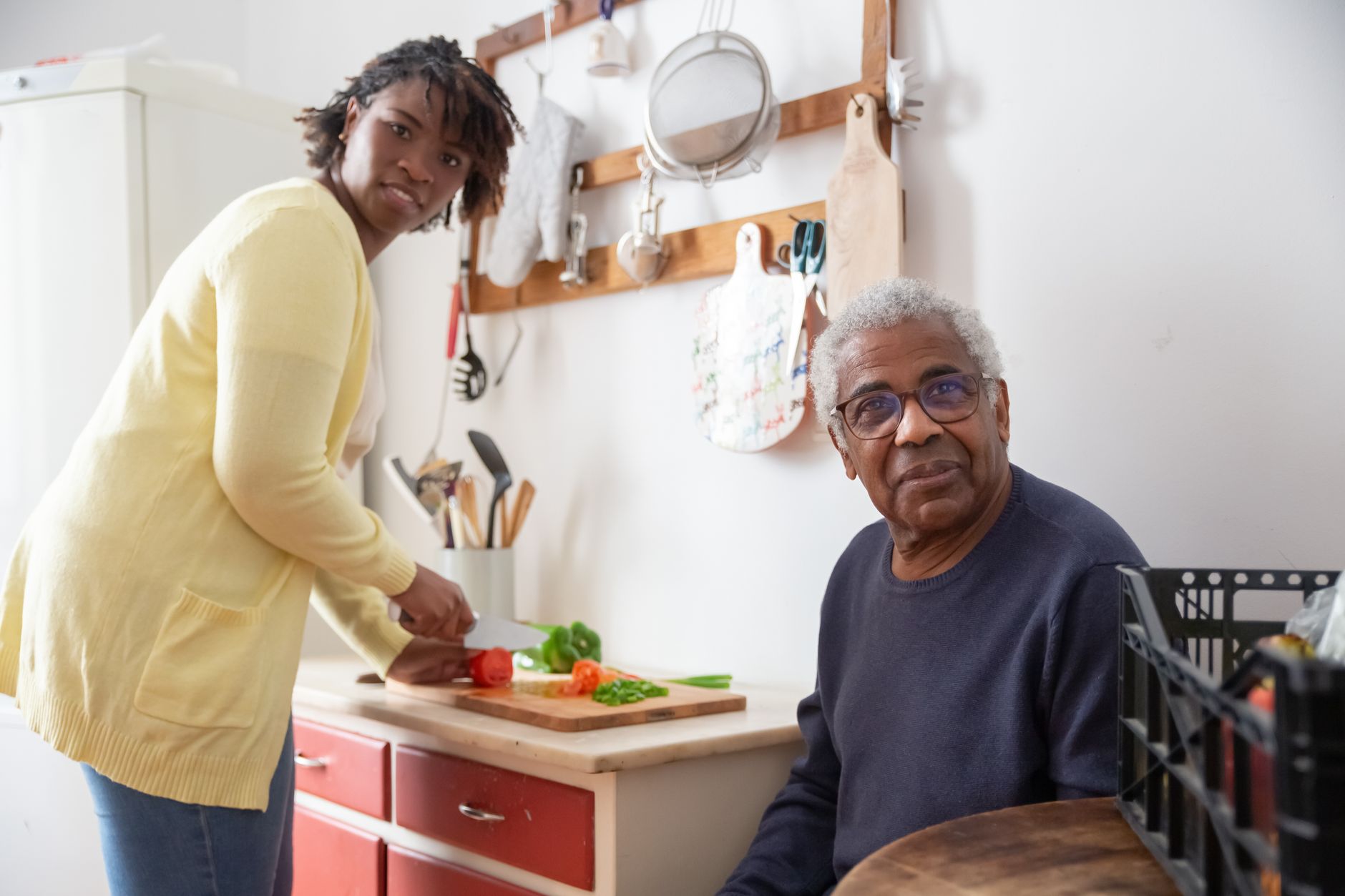 Older man seated in his kitchen while a support worker prepares a meal, showing mobile occupational therapy and aged care support at home in the Northern Rivers