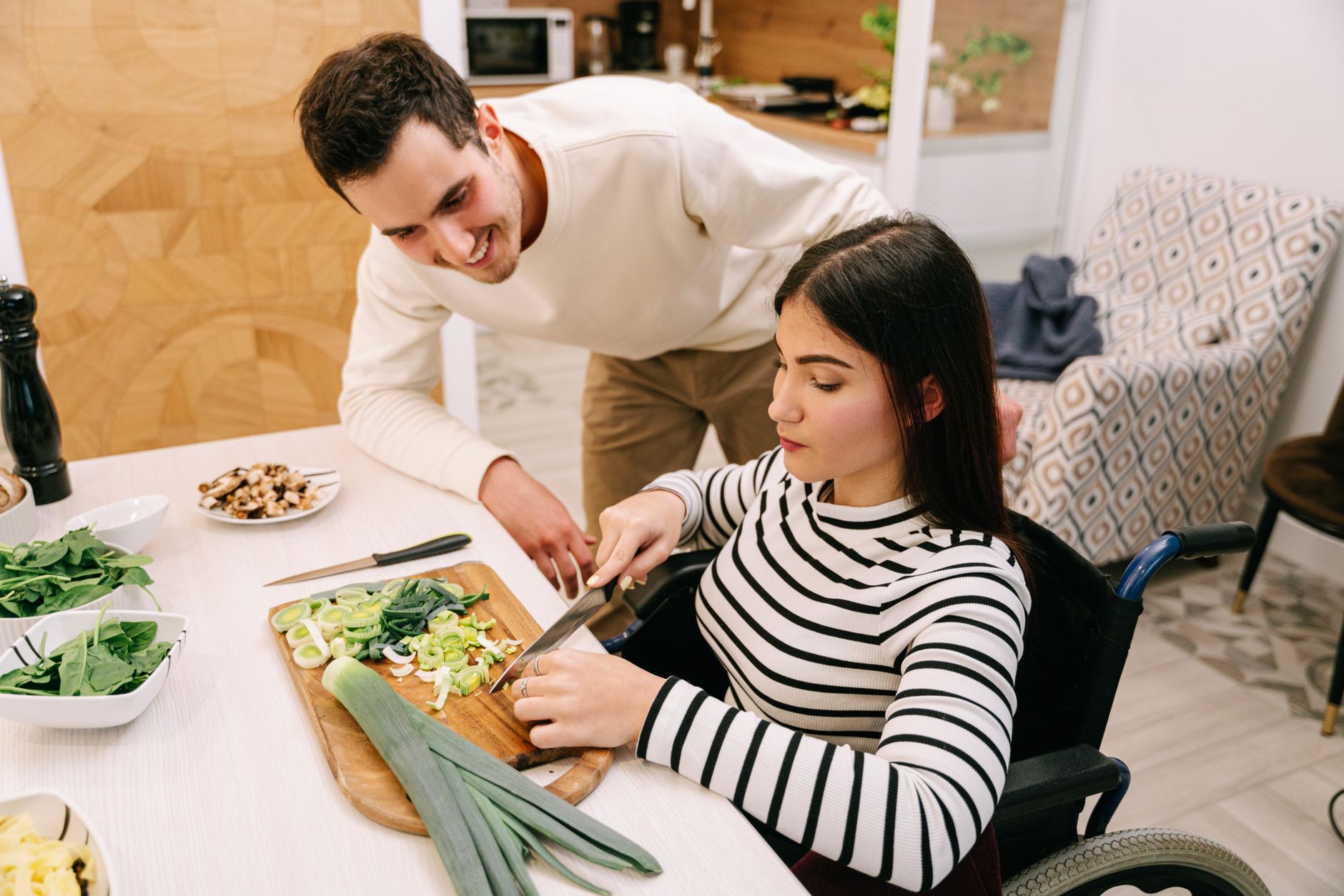 Woman using a wheelchair preparing a meal in her own kitchen with support alongside, showing the everyday independence occupational therapy in the Northern Rivers works towards