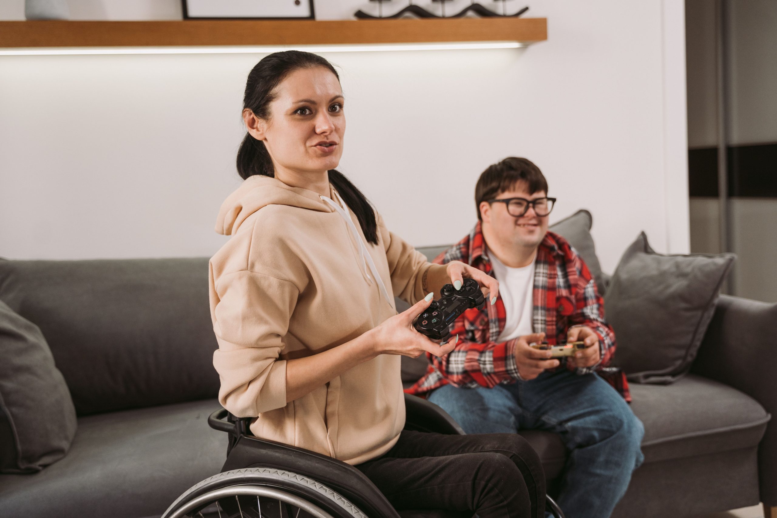 Two housemates in a shared home, one using a wheelchair, playing a video game together in their living room