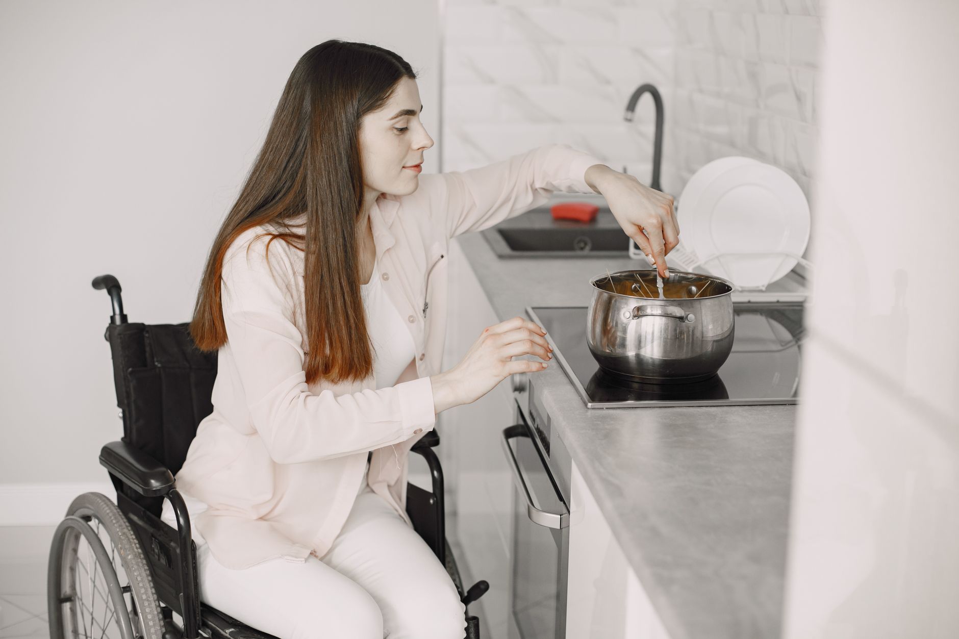 Woman using a wheelchair cooking a meal on the cooktop in her own kitchen